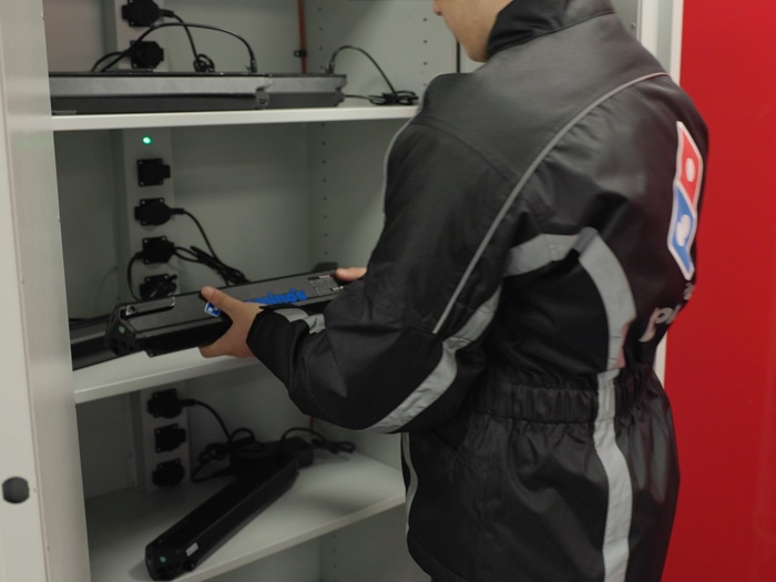 Medewerker Domino's Pizza legt accu van zijn bezorgfiets in Batteryguard accukast aan de lader